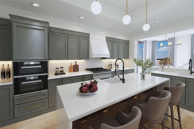 kitchen with light hardwood / wood-style floors, sink, a center island with sink, high end stove, and custom exhaust hood