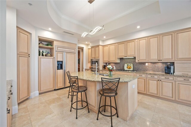 kitchen featuring a center island with sink, light stone countertops, light tile patterned floors, a tray ceiling, and built in appliances