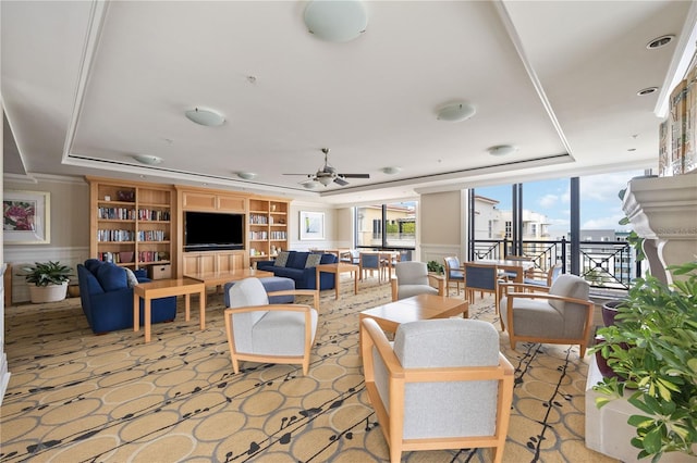 living area featuring ceiling fan, a wainscoted wall, and a raised ceiling