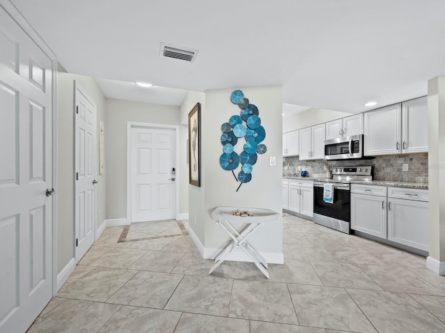 kitchen with decorative backsplash, white cabinetry, light tile patterned floors, and appliances with stainless steel finishes