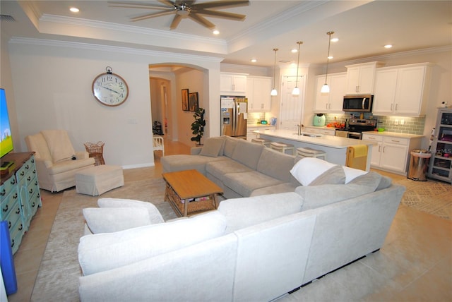 tiled living room with ceiling fan, sink, crown molding, and a tray ceiling