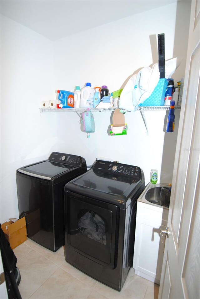 washroom with light tile patterned floors, washing machine and dryer, sink, and cabinets