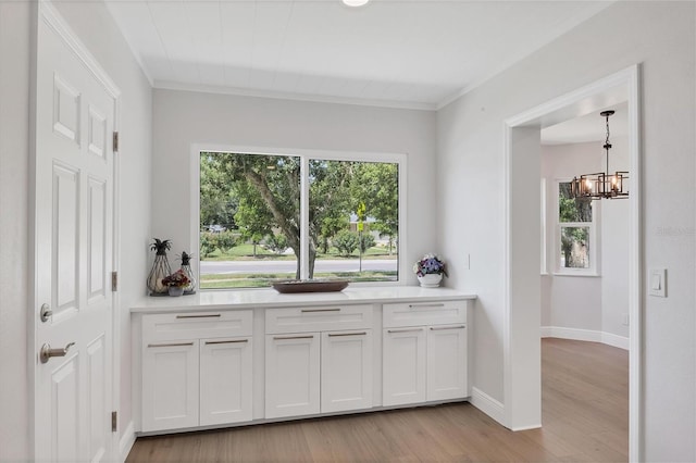 kitchen featuring light hardwood / wood-style flooring, decorative light fixtures, white cabinetry, ornamental molding, and a notable chandelier