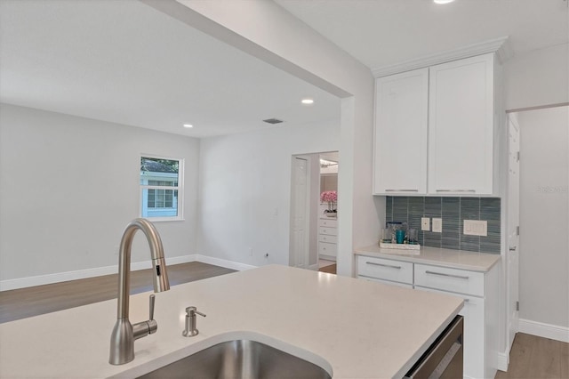 kitchen with sink, hardwood / wood-style flooring, stainless steel dishwasher, tasteful backsplash, and white cabinetry