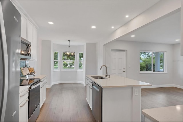 kitchen with sink, decorative light fixtures, light wood-type flooring, appliances with stainless steel finishes, and a center island with sink