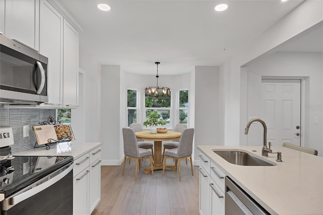 kitchen featuring hanging light fixtures, white cabinetry, appliances with stainless steel finishes, light hardwood / wood-style floors, and sink