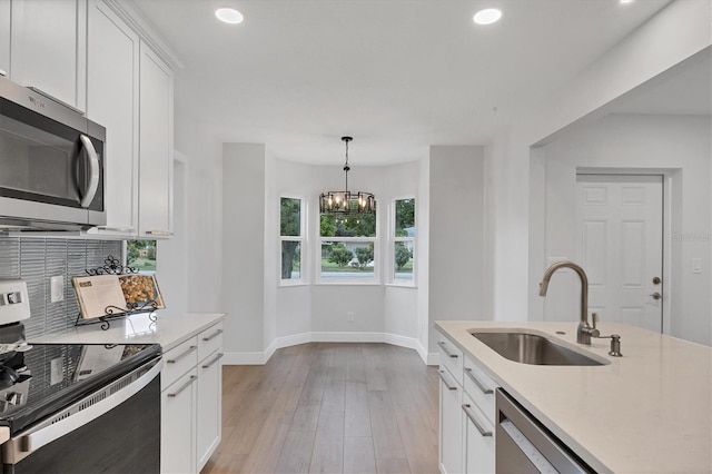 kitchen with stainless steel appliances, decorative light fixtures, light hardwood / wood-style flooring, sink, and white cabinets