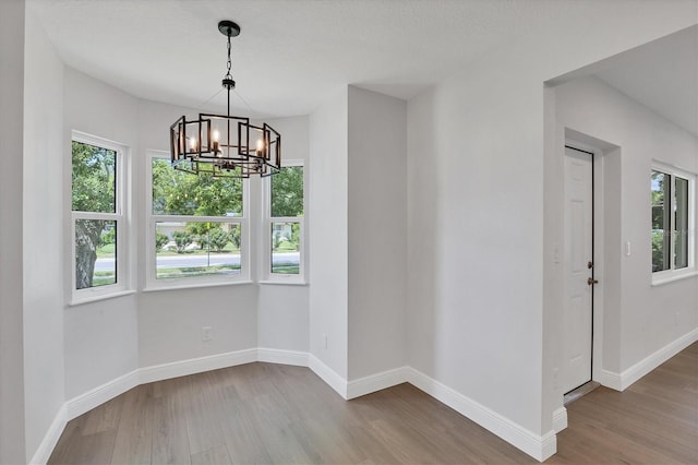 unfurnished dining area featuring hardwood / wood-style flooring, a notable chandelier, and a healthy amount of sunlight