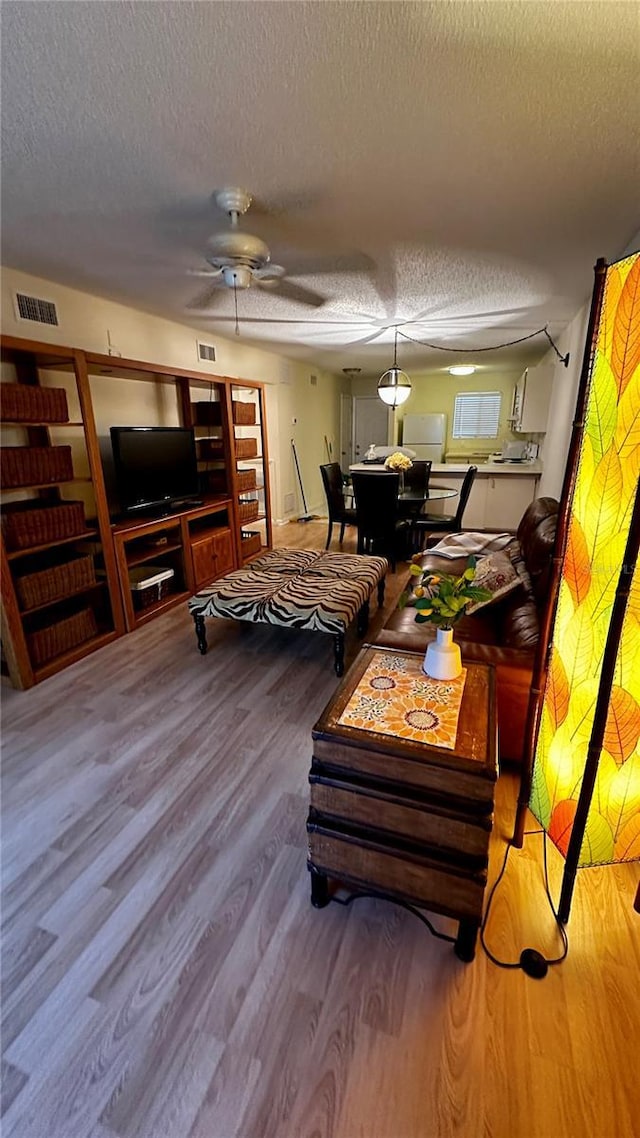 living area featuring a textured ceiling, wood finished floors, visible vents, and a ceiling fan