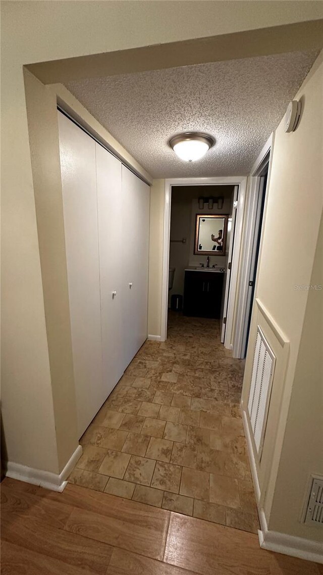 corridor featuring baseboards, visible vents, a sink, and a textured ceiling