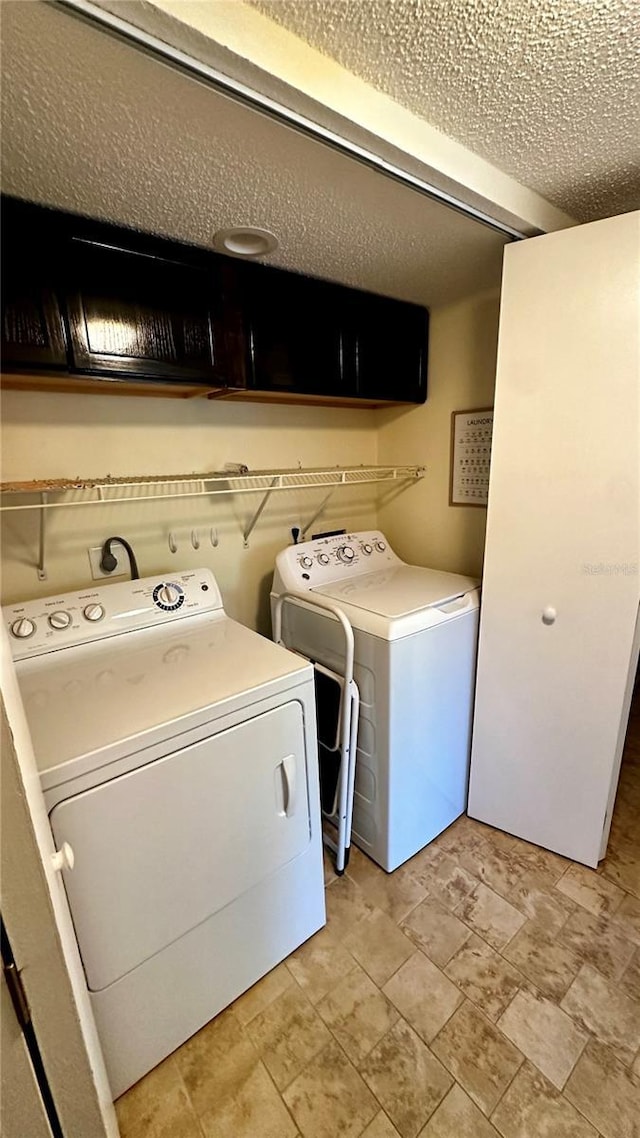 washroom with washer and dryer, cabinet space, and a textured ceiling