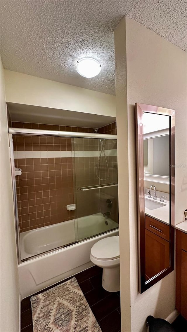 bathroom with combined bath / shower with glass door, a textured ceiling, toilet, and vanity