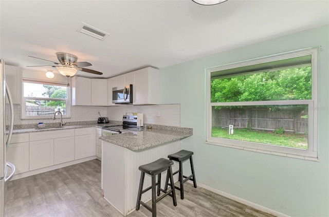 2900 Siesta Dr, Venice, FL 34293 - kitchen with visible vents, appliances with stainless steel finishes, white cabinetry, a peninsula, and a kitchen bar