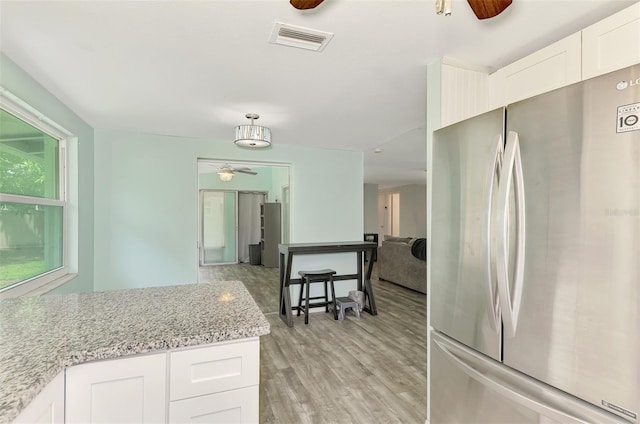 2900 Siesta Dr, Venice, FL 34293 - kitchen featuring visible vents, ceiling fan, freestanding refrigerator, light wood-style floors, and white cabinetry