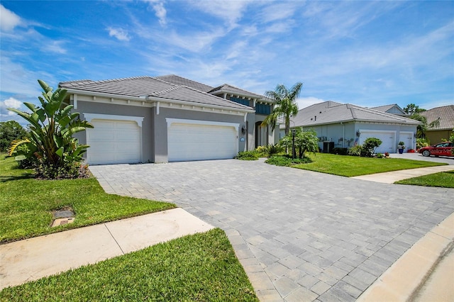 view of front of home with a garage, a tile roof, decorative driveway, a front lawn, and stucco siding