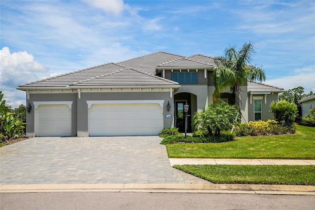 view of front of home with a garage, a tiled roof, decorative driveway, a front lawn, and stucco siding