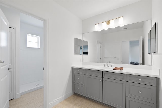 full bathroom with a tile shower, vanity, and baseboards