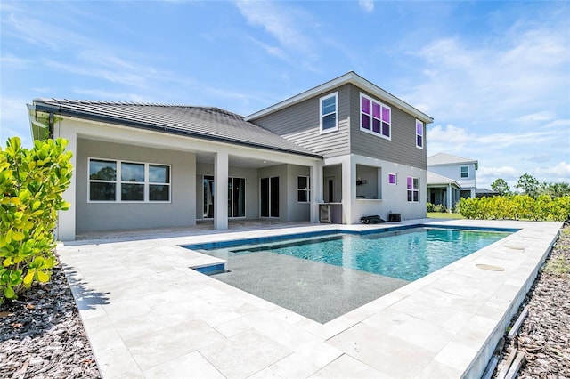 rear view of property featuring stucco siding, an outdoor pool, and a patio