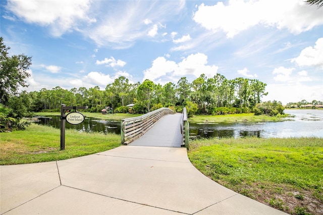 view of community with driveway, a lawn, and a water view