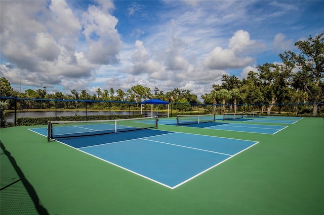 view of tennis court with a water view and fence