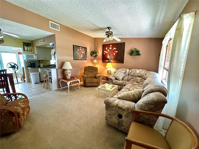 living area with visible vents, ceiling fan, light carpet, and a textured ceiling