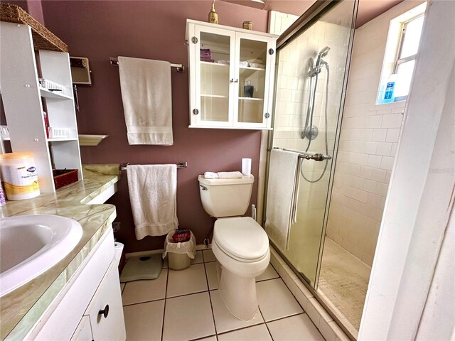 bathroom featuring a shower with door, toilet, vanity, and tile patterned floors