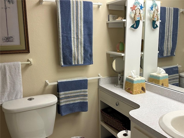 bathroom featuring toilet, a textured wall, and vanity