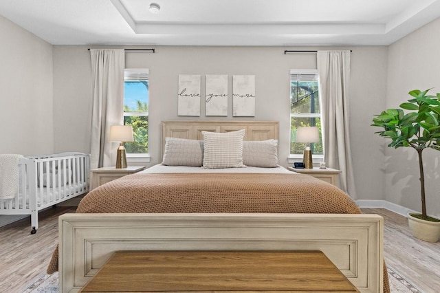 bedroom with light hardwood / wood-style flooring and a tray ceiling