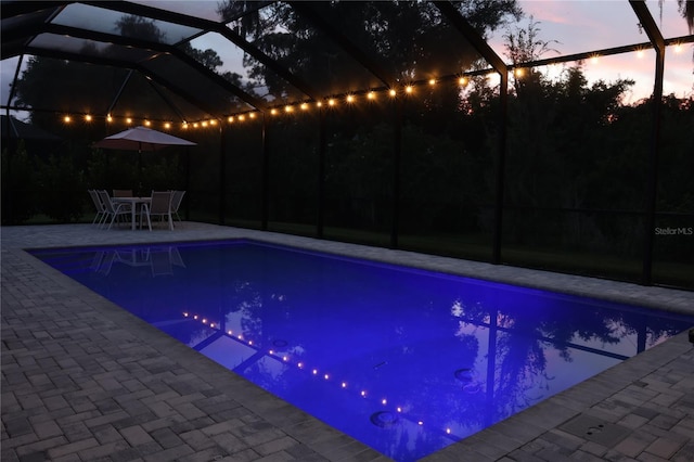 pool at dusk featuring a patio and glass enclosure