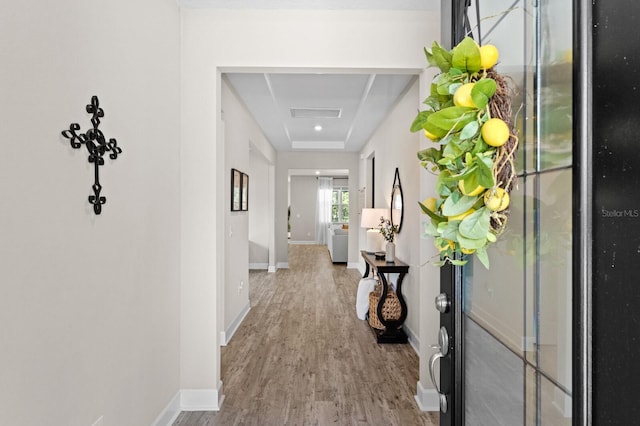 corridor with light hardwood / wood-style floors and a raised ceiling