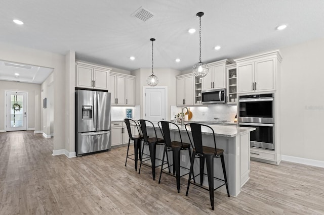 kitchen with an island with sink, appliances with stainless steel finishes, tasteful backsplash, a kitchen breakfast bar, and hanging light fixtures