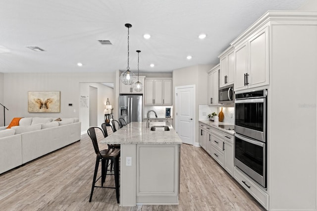 kitchen featuring a center island with sink, sink, white cabinetry, appliances with stainless steel finishes, and a breakfast bar area