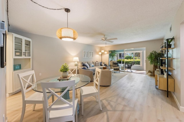 dining area with ceiling fan, light hardwood / wood-style flooring, and a textured ceiling