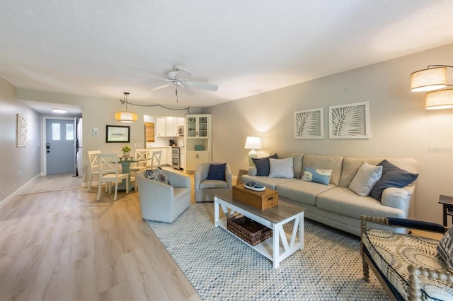 living room featuring ceiling fan, light hardwood / wood-style flooring, and a textured ceiling