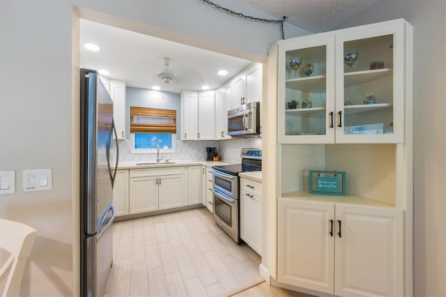 kitchen featuring sink, a textured ceiling, decorative backsplash, white cabinets, and appliances with stainless steel finishes