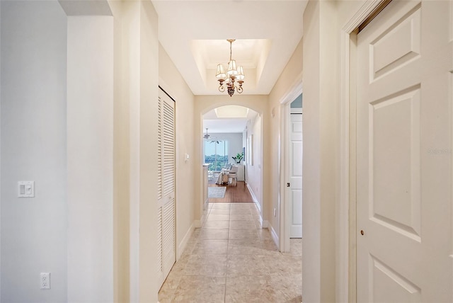 hall featuring a raised ceiling, an inviting chandelier, and light hardwood / wood-style floors