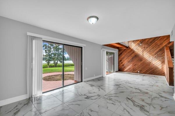 1502 NE Buckeye Rd NE Unit 2, Winter Haven, FL 33881 - unfurnished living room featuring marble finish floor, an accent wall, wooden walls, and baseboards