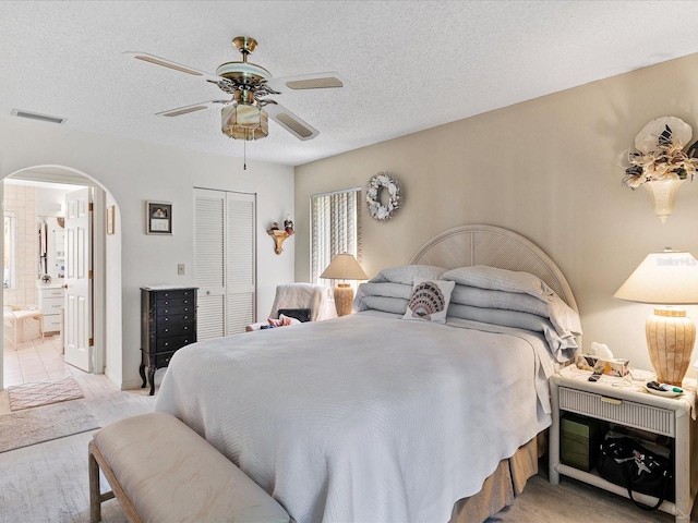 bedroom featuring light tile patterned flooring, a closet, connected bathroom, a textured ceiling, and ceiling fan