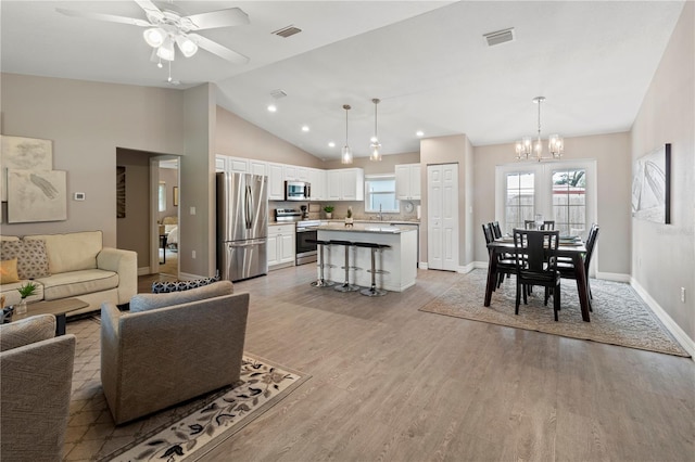 living room featuring lofted ceiling, ceiling fan with notable chandelier, and light wood-type flooring