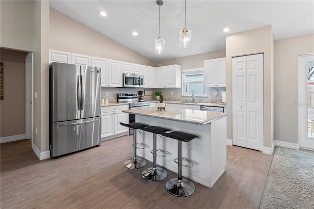 kitchen featuring pendant lighting, appliances with stainless steel finishes, white cabinetry, light stone counters, and a kitchen island