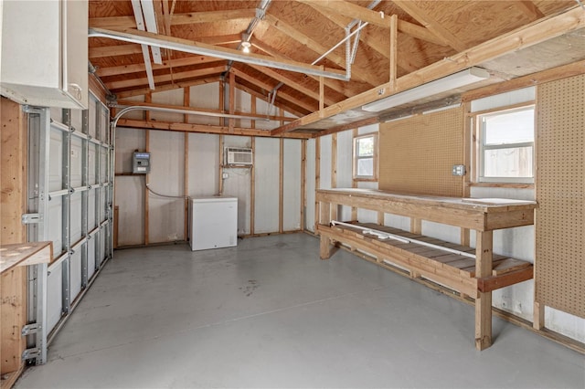 basement featuring a wall unit AC, a workshop area, and refrigerator