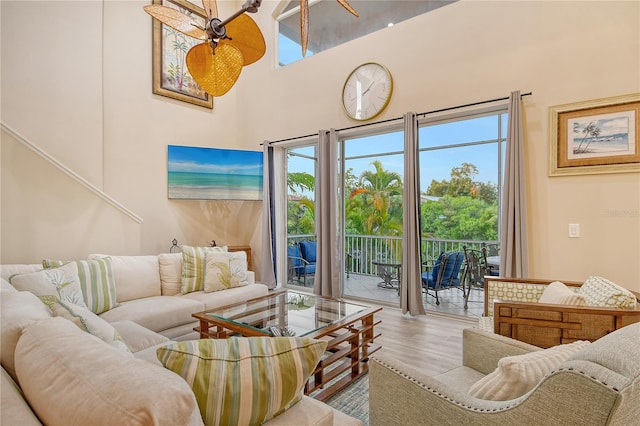 living room featuring ceiling fan, a high ceiling, and light hardwood / wood-style flooring