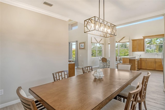 dining space with a notable chandelier, crown molding, light hardwood / wood-style floors, and a high ceiling