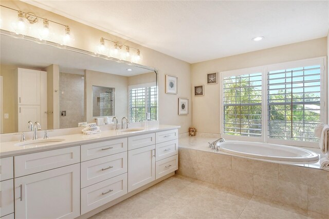 bathroom with tile patterned flooring, tiled tub, and dual vanity