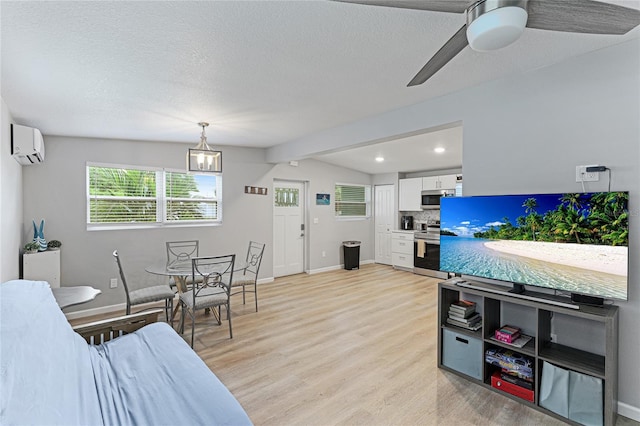 living room featuring light wood finished floors, baseboards, a textured ceiling, and a wall mounted air conditioner