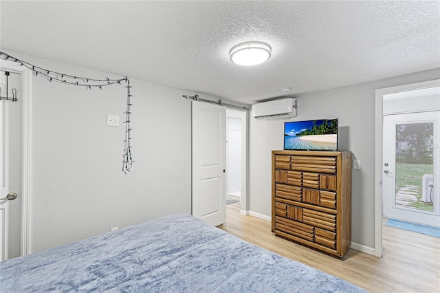 bedroom with a wall mounted AC, a barn door, a textured ceiling, light wood-type flooring, and baseboards