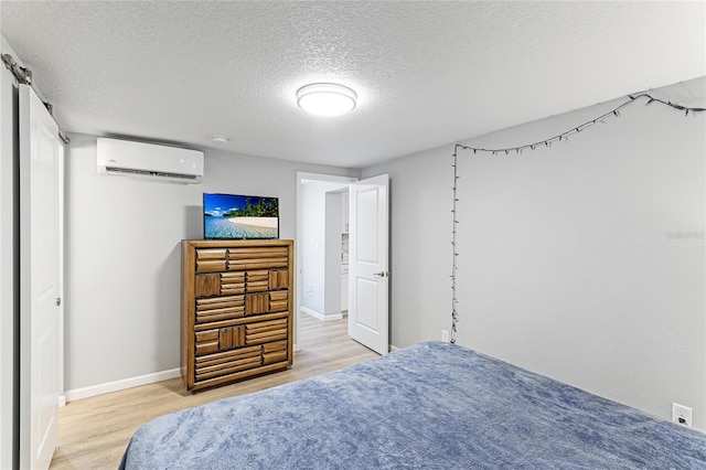 bedroom with a textured ceiling, an AC wall unit, light wood-type flooring, and baseboards