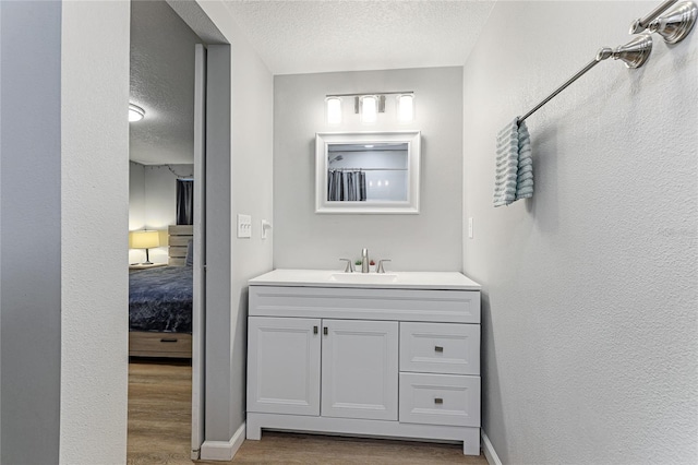 full bathroom with a textured wall, vanity, a textured ceiling, wood finished floors, and baseboards