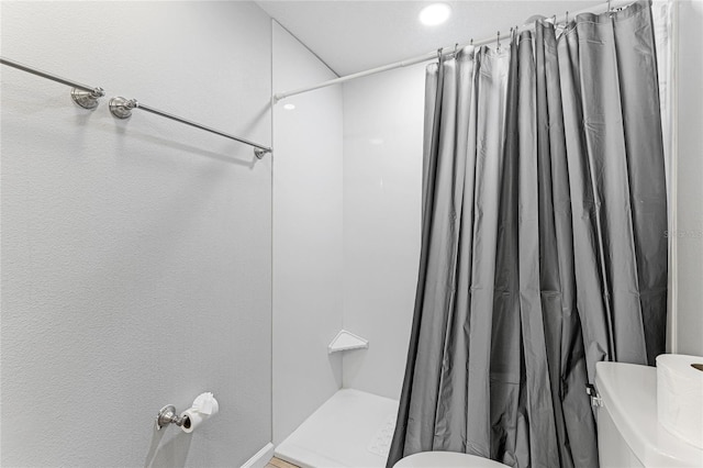 full bathroom with a shower with curtain, a textured wall, and toilet