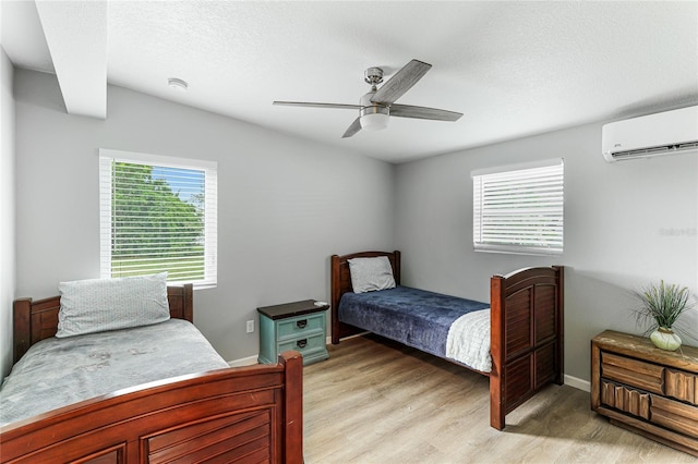 bedroom featuring light wood-style floors, a ceiling fan, a textured ceiling, a wall mounted air conditioner, and baseboards